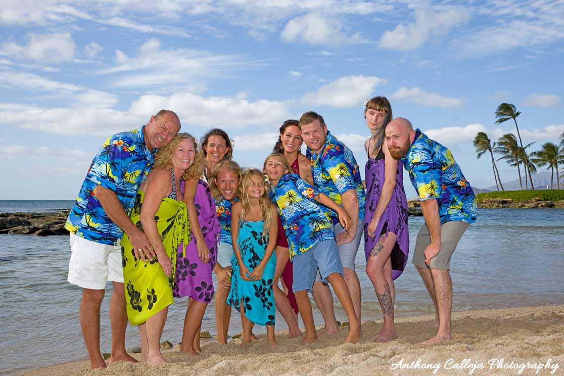 Portrait of a family of ten making funny faces wearing Hawaiian attire at Paradise Cove Beach Koolina